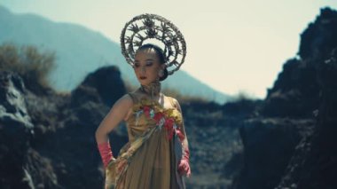 Yan tarafa bakan Endonezyalı bir dansçının orta boy fotoğrafı. Ağır altın bir taç takıyor, kolye, ve çiçekli altın bir elbise, bulanık kayalık bir arka planda geçiyor..