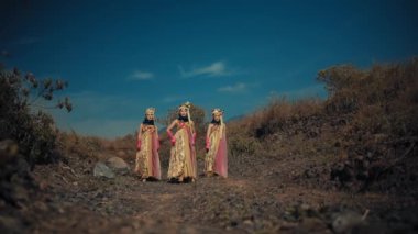Renkli elbiseli geleneksel kadınlar gün ışığında açık mavi gökyüzünün altında kırsal bir yolda yürüyorlar.