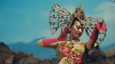 Endonezyalı zarif bir kadın geleneksel dans figürlerini sergiliyor, rüzgarda şeffaf renkte bir şal sallıyor altın takıyor ve başlık takıyor..