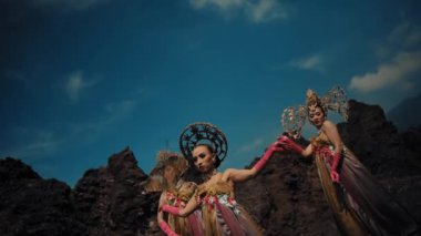 Volkanik arazide dans eden egzotik kostümlü bir kadın. Arka planda gün ışığında dramatik bir gökyüzü.