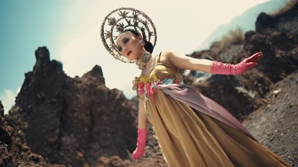 日光の間に劇的な火山の風景にポーズする伝統的な衣装とヘッドドレスの優雅な女性 — ストック動画