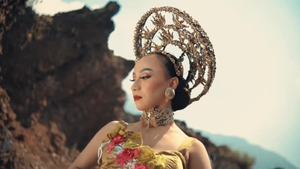 明るい空の下の岩の風景に立って飾られたヘッドピースで伝統的な服装のエレガントな女性 — ストック動画
