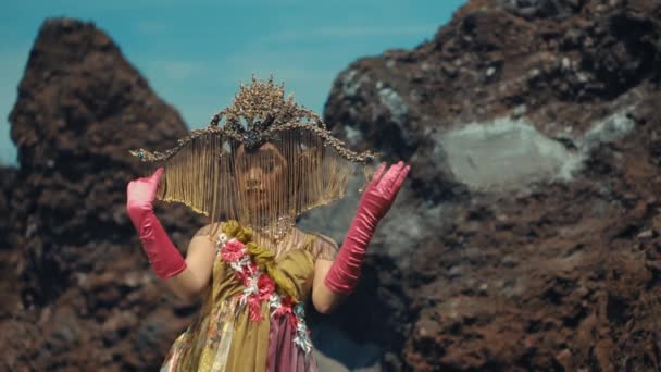 身着异国情调服装头戴帽子的女人白天站在火山岩旁边 — 图库视频影像