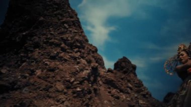 Gündüz vakti dramatik bir gökyüzü altında kayalık bir oluşum tarafından poz veren eşsiz elbiseli zarif bir kadın.