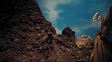 Gündüz vakti dramatik bir gökyüzü altında kayalık bir oluşum tarafından poz veren eşsiz elbiseli zarif bir kadın.