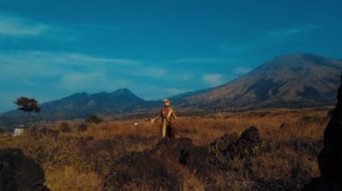 Uçsuz bucaksız bir tarlada duran gezgin. Arka planda dağlar. Gün ışığında macera ve keşif hissi uyandırıyor.