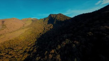 Gün batımında gölgeler ve gün ışığında sıcak bir ışıkla engebeli bir dağ manzarası.