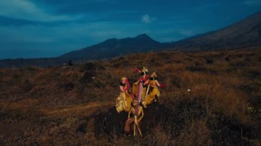 Geleneksel canlı kostümlü atlı adam alacakaranlıkta dağlarla manzaralı bir arazide at sürüyor..