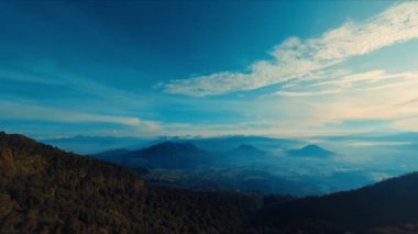 Gün ışığında açık mavi gökyüzünün altında yemyeşil bir dağ sırtı görünüyor.
