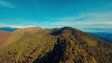 Gün ışığında berrak mavi gökyüzü olan yemyeşil bir dağ sırtı.