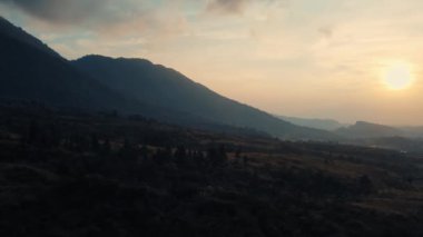 Yumuşak ışık ve gölgeli sakin bir dağ manzarasının üzerinde gün batımı, arka plan veya gündüz doğa temaları için idealdir.