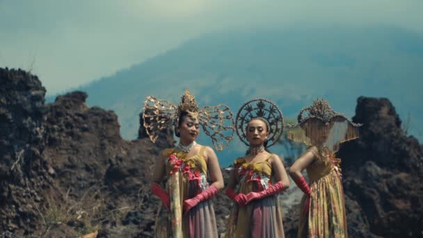 バリ島の伝統的な服装の2人の女性が昼間の背景に火山の風景で文化的なダンスを行います — ストック動画