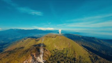 Bereketli yeşil dağ manzarası açık mavi gökyüzünün altında uzak bir şelale gün ışığında.