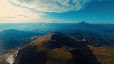 Uçsuz bucaksız mavi gökyüzünün altındaki yemyeşil yemyeşil tepelerin gün ışığında hafif bulutlarla çevrili görüntüsü.