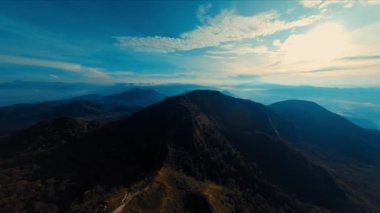 Açık mavi gökyüzünün altındaki yemyeşil bir dağ sırtı gün ışığında nefes kesici bir hava manzarası.