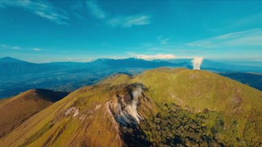Açık mavi gökyüzünün altındaki yemyeşil bir dağ sırtı gün ışığında nefes kesici bir hava manzarası.