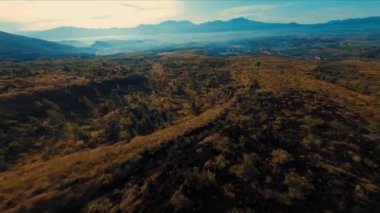 Dalgalanan arazisi ve sisli bir gökyüzünün altındaki uzak dağların engebeli manzarası..