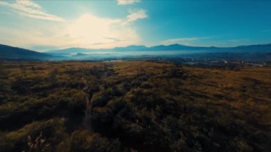 Güneşin doğuşuyla birlikte geniş bir tarlaya ve gün ışığında uzak dağlara düşen altın ışıkla süpürülen manzara.