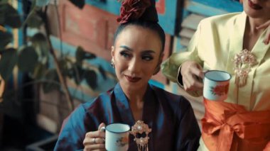 Geleneksel Asya kıyafetli iki kadın gündüz vakti birlikte çay içiyorlar.