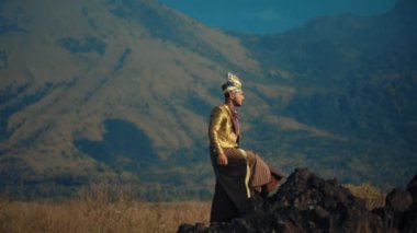 Geleneksel kıyafetli bir adam gün ışığında dağ zemininde ayakta duruyor.