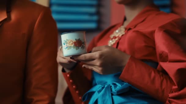 装飾的なカップを保持する赤いドレスのエレガントな女性は 日光の間に手とカップに焦点を当てています — ストック動画