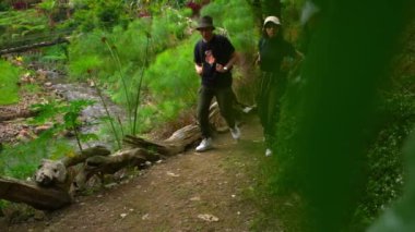 Genç bir çift nehir kenarında yürüyüş yaparken soluklanmak için durur. Adam şapkasıyla yüzünü yelpazeliyor ve kadın yorgun bir şekilde öne eğiliyor..