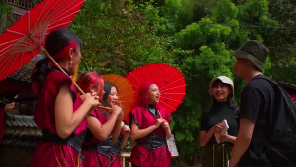 游客与当地妇女在白天穿着传统服饰 手持红色雨伞进行互动 — 图库视频影像