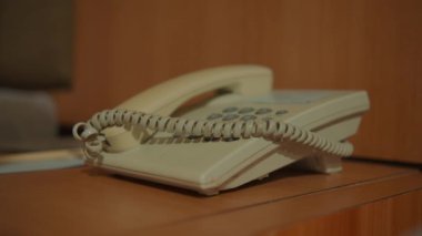Sabit telefon ve not defteriyle bir otel komodininin statik görüntüsü konuk odalarında sunulan kolaylık ve hizmeti vurgular..