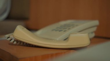 Standart bir beyaz ofis ya da otel telefonunun detaylı görüntüsü. Parlak ahşap bir yüzey üzerinde oturuyor. İletişim ve bağlantıyı temsil ediyor..