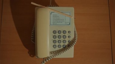 Yatağın başucundaki komodinden beyaz bir sabit telefonun telefonunu almak için uzanan bir elin yan görüntüsü..