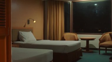 Geceleri rahat bir otel odası, rahat bir yatak, masa, lamba ve gece boyunca perdeleri olan bir pencere.