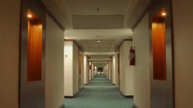 Her iki tarafında da kapılar olan loş bir otel koridoru ve otelin içinde kaybolan bir yere giden halı döşeli bir zemin.