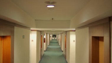 Boş otel koridoru simetrik kapılar ve halı döşeli, gece boyunca tavan lambalarıyla aydınlatılmış.