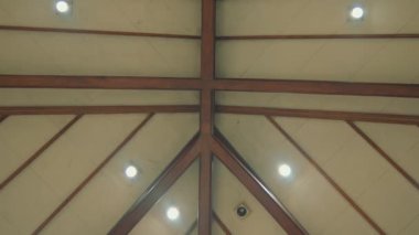 Düşük açılı bir çekim, beyaz tavana karşı koyu ahşap kirişlerin geometrik desenini gösteriyor..
