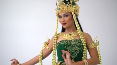 Geleneksel Endonezya Siger tacı takan ve yeşil kadife giyinen bir dansçı kameraya doğru zarif bir şekilde uzanır..