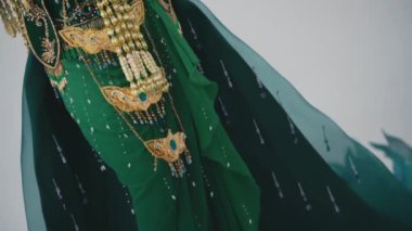 Altın işlemeli ve mücevherli zarif geleneksel yeşil elbise. Beyaz stüdyo içinde kültürel moda sergileniyor.
