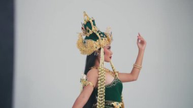 Geleneksel Balili dans kostümü giyen, karmaşık altın başlıklı bir kadın, sabahları gri arka planda dans jesti yapıyor.