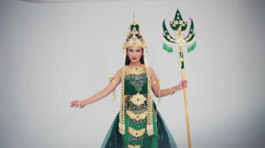 Geleneksel Tayland kostümlü, başlıklı, yeşil elbiseli, elinde dekoratif bir personel sabah beyaz arka planda poz veren bir kadın.