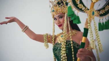 Geleneksel Balili dansçı kostümlü, altın başlıklı, yeşil elbiseli, gün ışığında zarif el hareketleriyle gösteri yapan bir kadın.