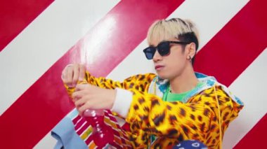 Leopar desenli ceketli ve güneş gözlüklü moda bir adam kırmızı ve beyaz çizgili arka planda ferahlatıcı bir pembe soda şişesi açıyor..