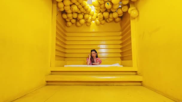 Menina Vestido Rosa Sentado Escadas Amarelas Cercado Por Esferas Amarelas — Vídeo de Stock