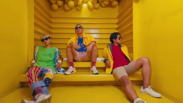 三个穿着五颜六色衣服的时尚人在黄色的楼梯上摆姿势 在早上散发着一股清凉而时尚的气息 — 图库视频影像