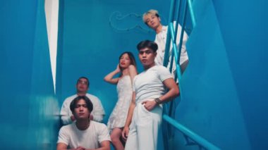 Mavi bir merdivende soğukkanlı poz veren beş genç Asyalı arkadaş. Beyaz kıyafetler giyiyorlar, moda editörü ya da modaya uygun estetik müzik grubu gibi görünüyorlar..