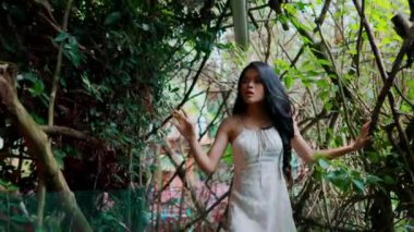 Çiçekli kıyafetli genç bir bayan, doğal sarmaşık kemerleriyle çevrili bir patika boyunca yavaşça yürüyor, tema parkının huzurlu atmosferinin tadını çıkarıyor..