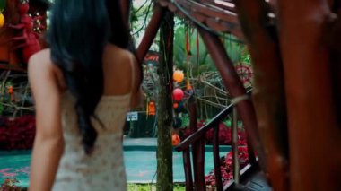 Süslü bir bahçede, kırsal ahşap bir yapıda yürüyen uzun saçlı bir kadını takip etmek. Kamera onun hareketlerini arkadan takip ediyor..