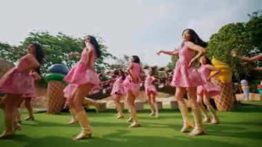 Pembe elbiseli bir grup çocuk güneşli bir günde dışarıda neşeyle dans ediyor, sabah boyunca özgürlük ve mutluluk ifade ediyorlar.