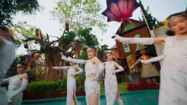 Geleneksel beyaz kostümlü, sarı başlıklı dansçılar gün ışığında bir açık hava kültür festivalinde gösteri yapıyorlar.