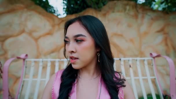 身穿粉红连衣裙的年轻女子坐在秋千上 背靠着土墙 面带微笑 — 图库视频影像