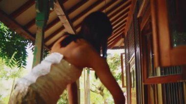 Geleneksel ahşap bir evin balkon alanını düzenleyen etnik Cava kıyafetli bir kadının düşük açılı görüntüsü..