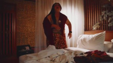 Etnik giyinmiş bir kadının portresi ev işlerini bitirdikten sonra bir yatak odasında dikilip iç çekerken bitkin görünüyor..